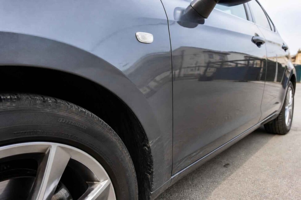 Przedni bok grafitowego samochodu Zbliżenie na przednie koło, drzwi i błotnik grafitowego samochodu na parkingu